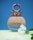 A perfume bottle with a unique metallic design at the top, against a blue background. The bottle is labeled 'Colors' and is positioned on a yellow surface. A white flower is placed next to it.