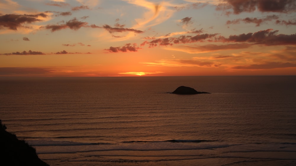 silhouette of rock formation on sea during sunset