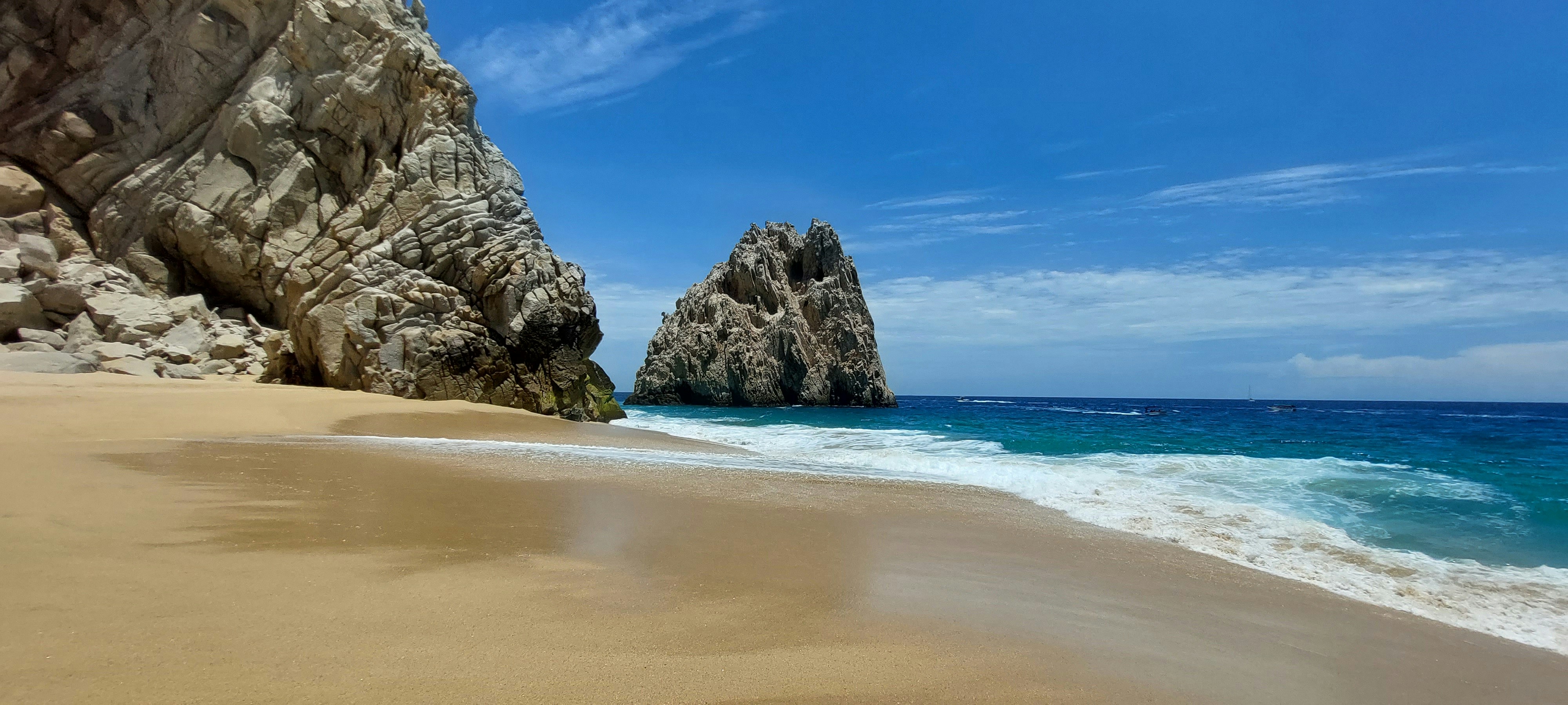brown rocky mountain beside blue sea under blue sky during daytime
