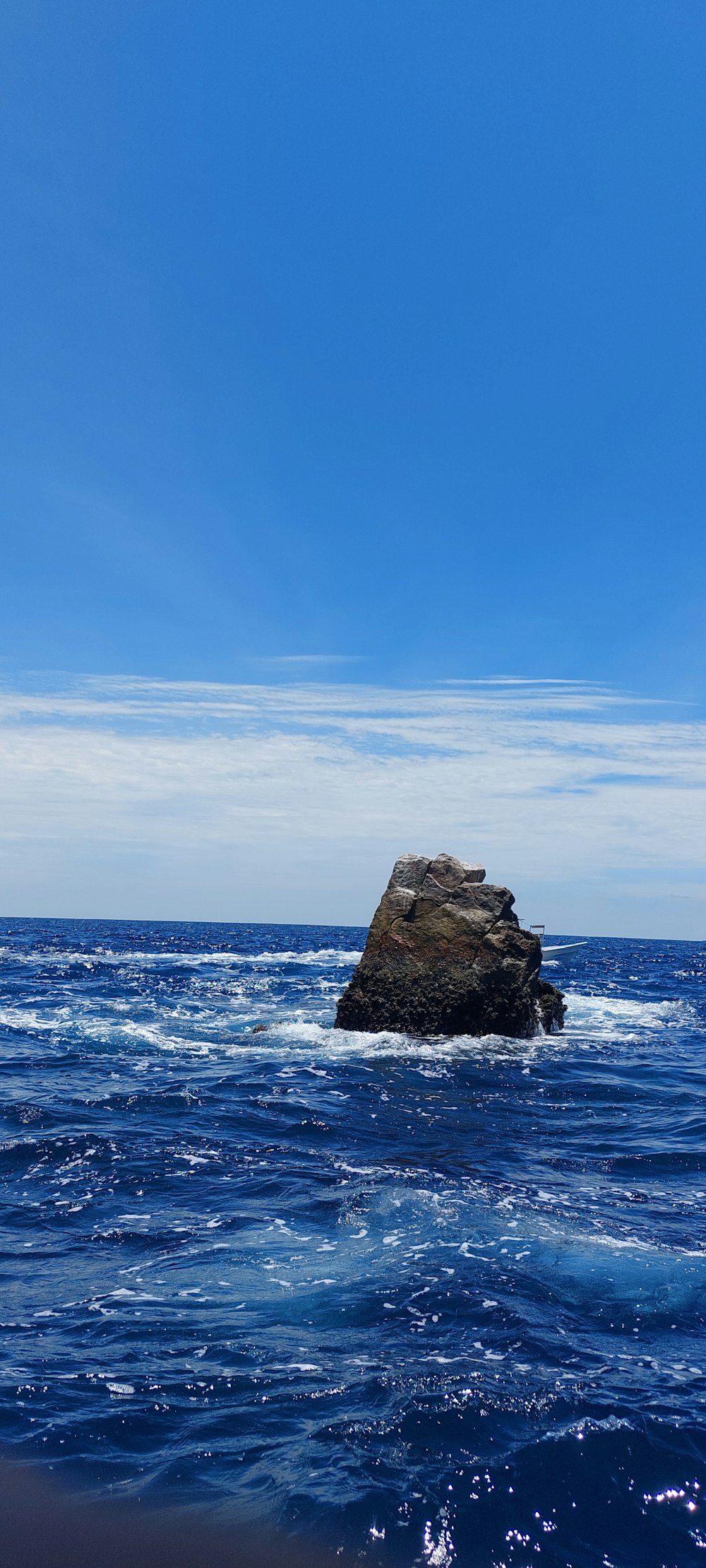 昼間の青空の下の海に浮かぶ茶色の岩層