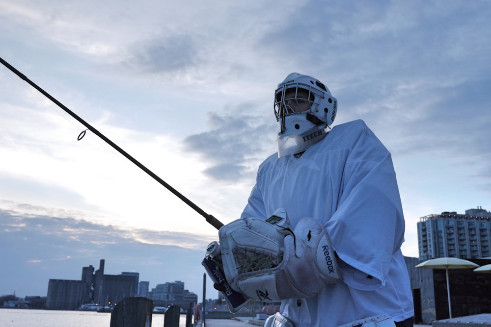 person in white jacket wearing white helmet holding black fishing rod