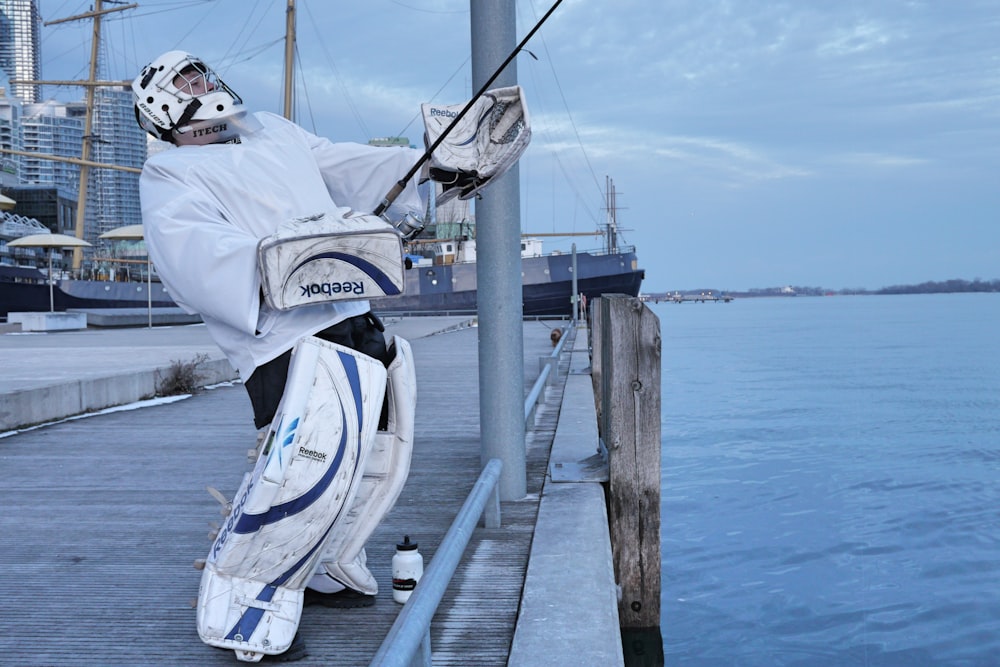 man in white long sleeve shirt and blue denim jeans sitting on wooden dock during daytime