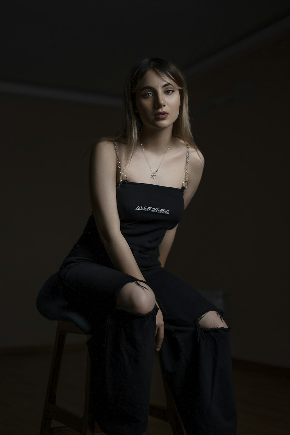 woman in black spaghetti strap top and black pants sitting on black chair