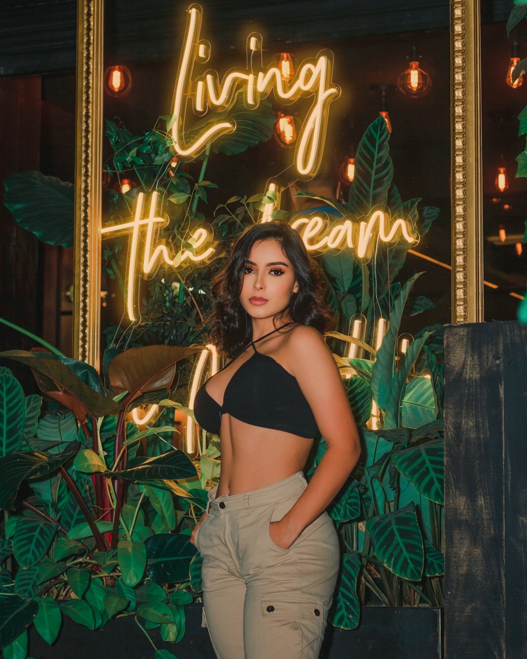 woman in black brassiere and white pants standing beside green plants