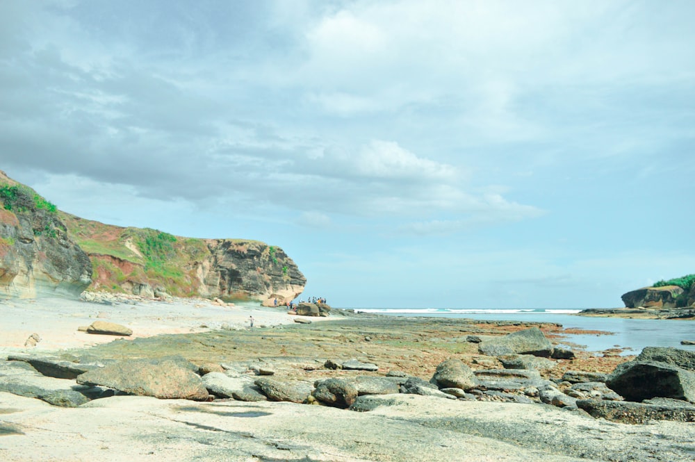 brown rock formation on sea shore under white clouds and blue sky during daytime