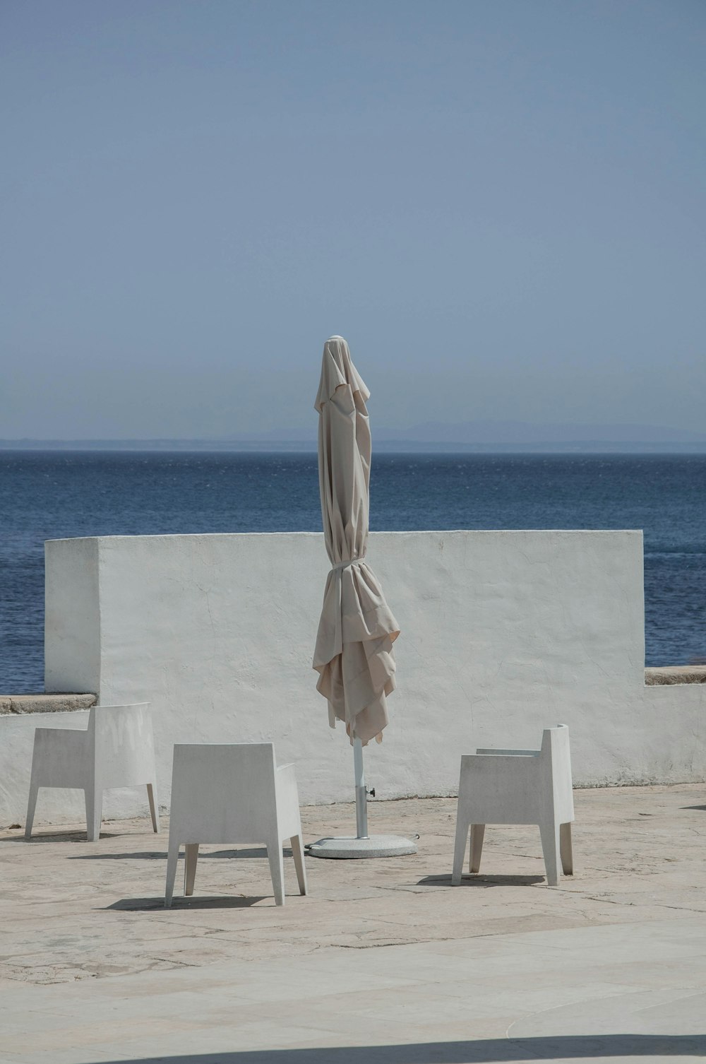 낮 동안 푸른 바다 근처의 흰색 콘크리트 테이블에 흰색과 갈색 우산
