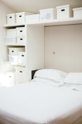 white bed linen near white wooden cabinet