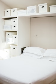 white bed linen near white wooden cabinet