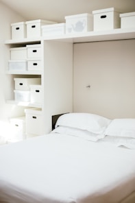 white bed linen near white wooden cabinet
