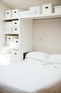 white bed linen near white wooden cabinet