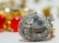A sparkling heart-shaped diamond surrounded by smaller round diamonds on a silver setting, with an out-of-focus background featuring vibrant red and yellow hues from blurred ornaments.