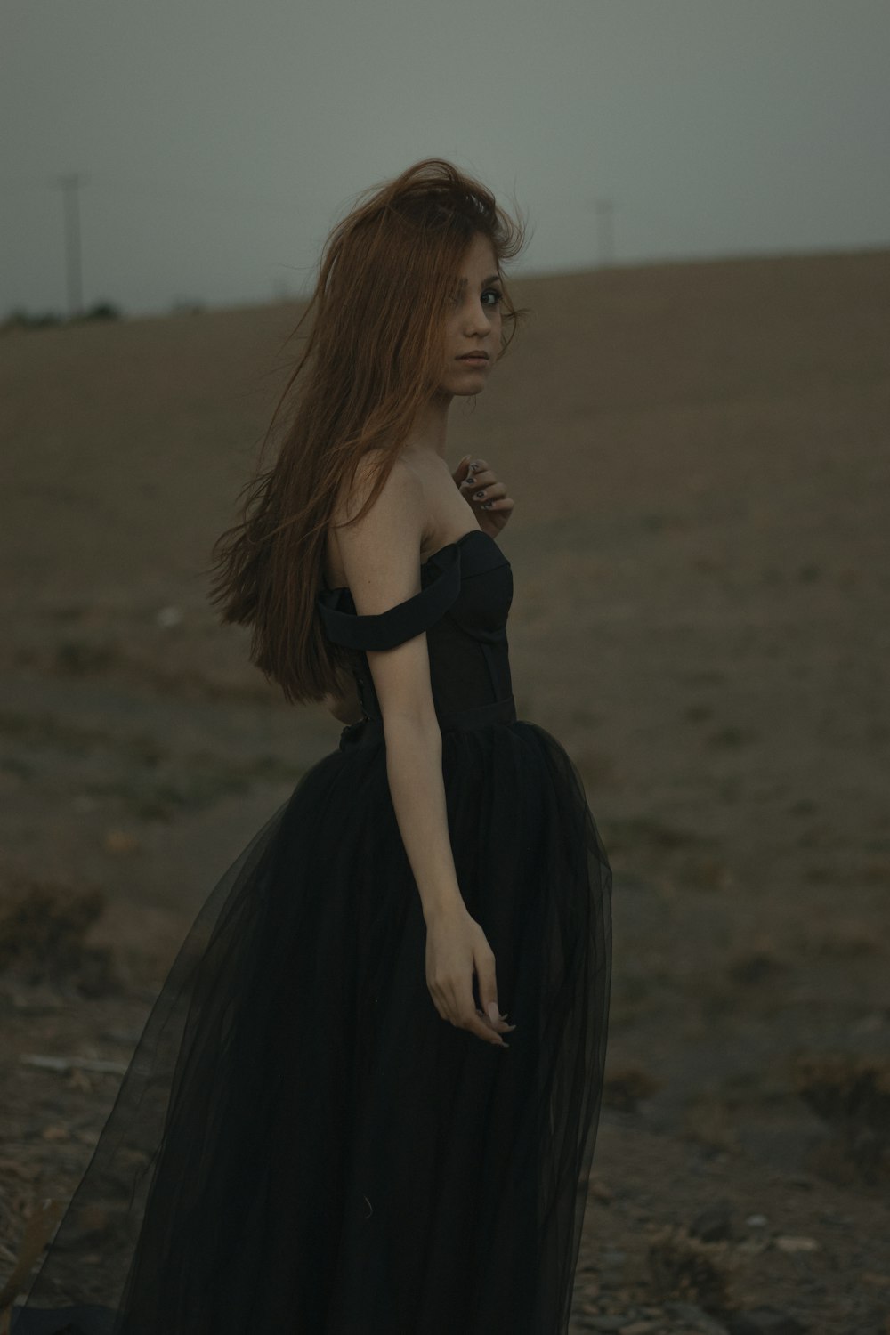 femme en robe noire debout sur un champ brun pendant la journée