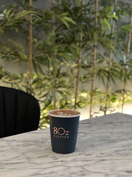 A serene cup of kopi jelly coffee on a wooden table surrounded by green plants, evoking a peaceful forest atmosphere.