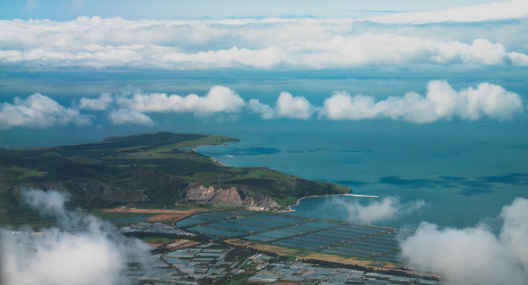 aerial view of green and brown mountains and body of water under blue and white cloudy
