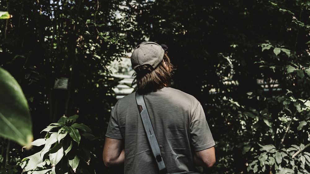 man in gray polo shirt and gray cap standing near green trees during daytime