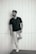man in black crew neck t-shirt and white pants standing beside white wall