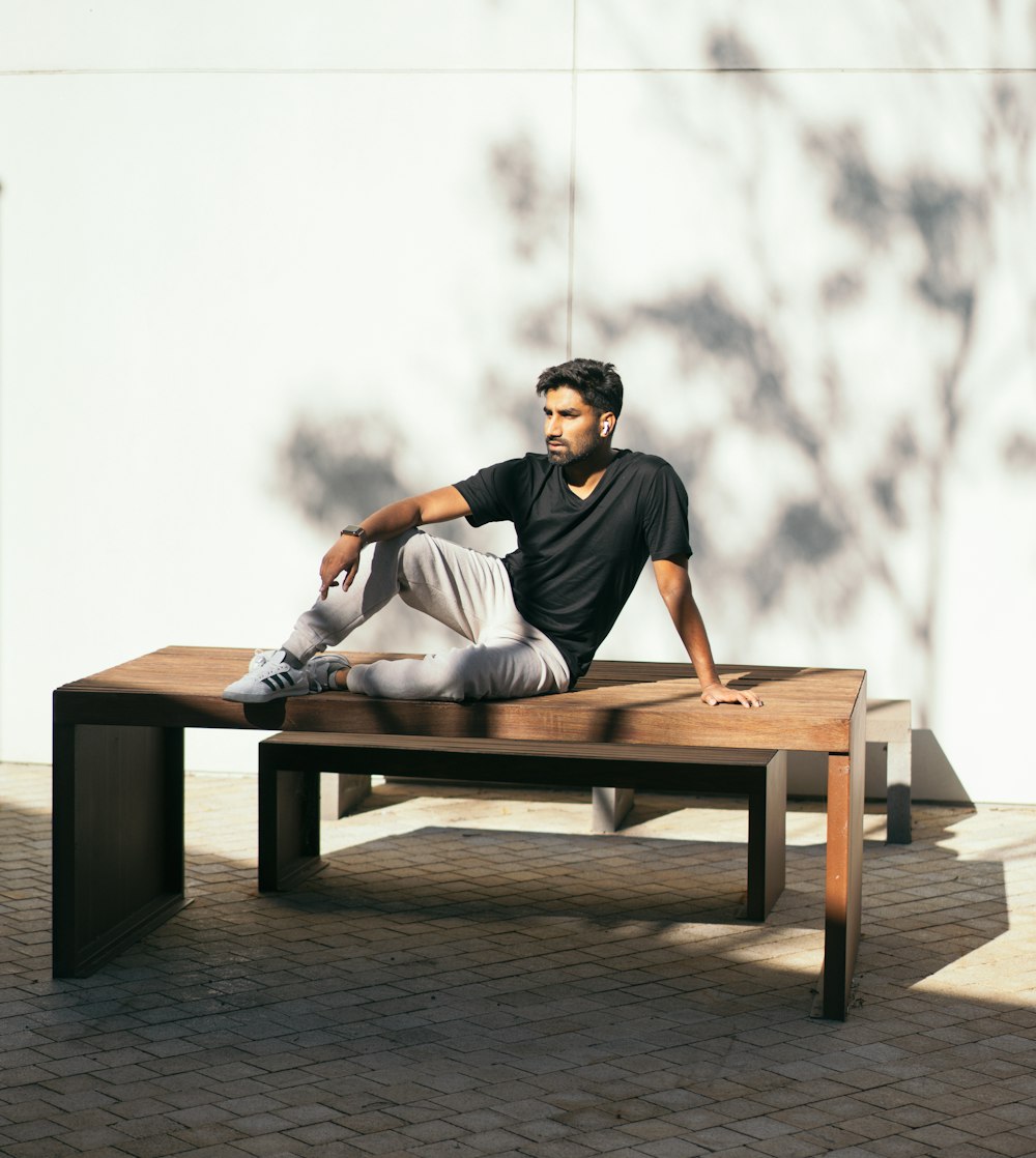 man in black crew neck t-shirt sitting on brown wooden bench