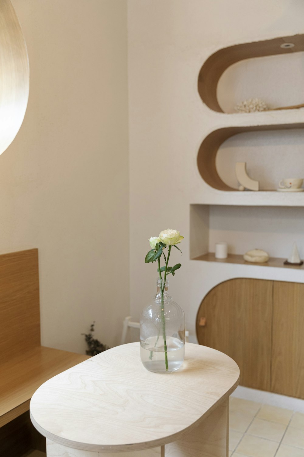 white roses in clear glass vase on white wooden shelf