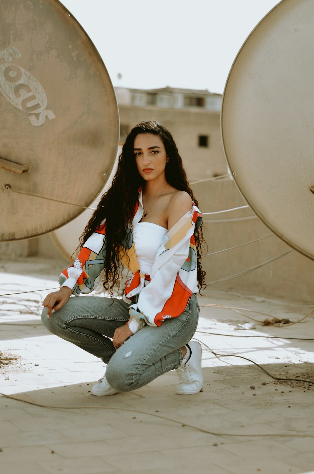 woman in white and red floral shirt and blue denim jeans sitting on concrete floor during