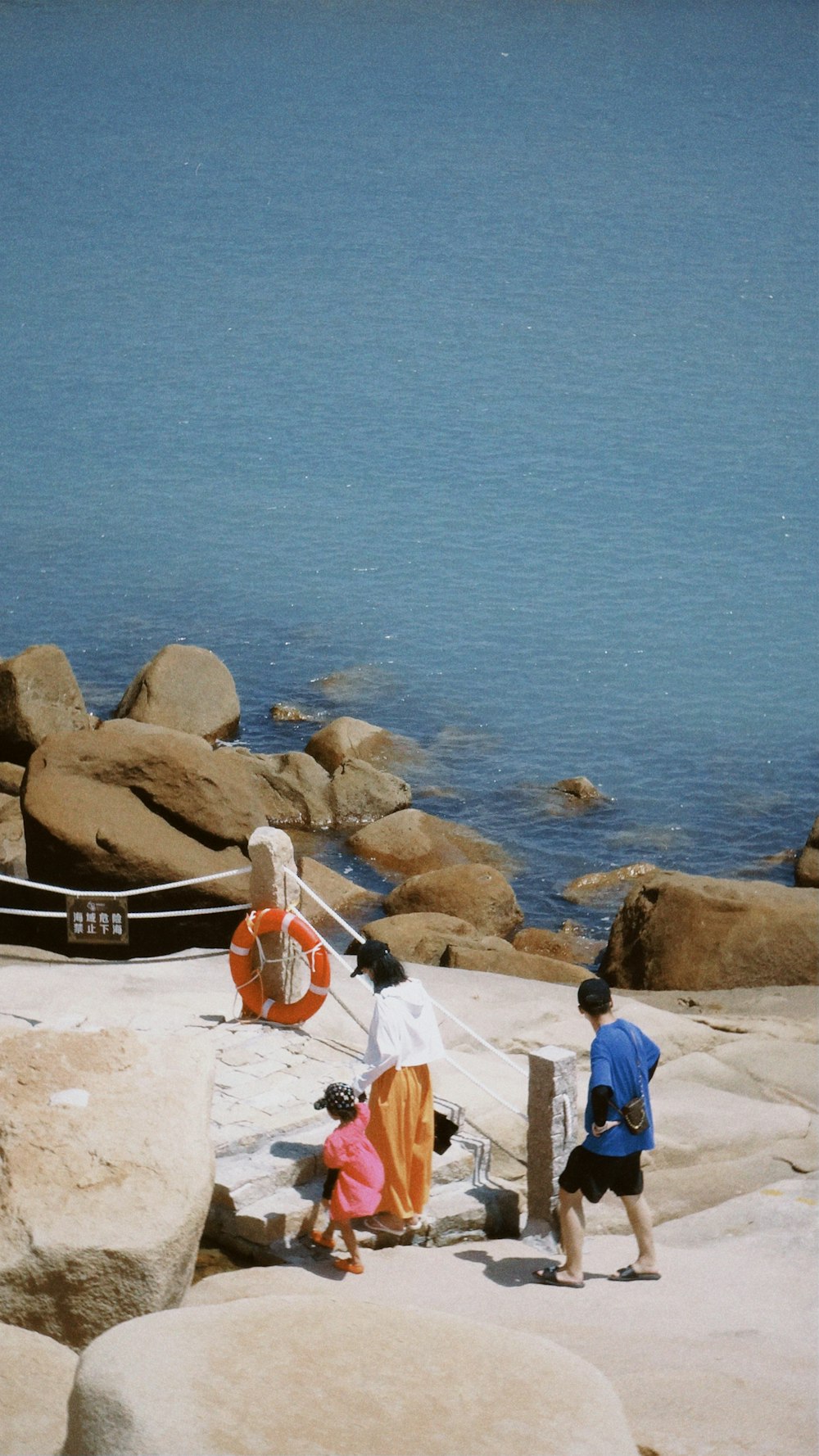 man in blue shirt and brown shorts standing on brown rock formation near body of water