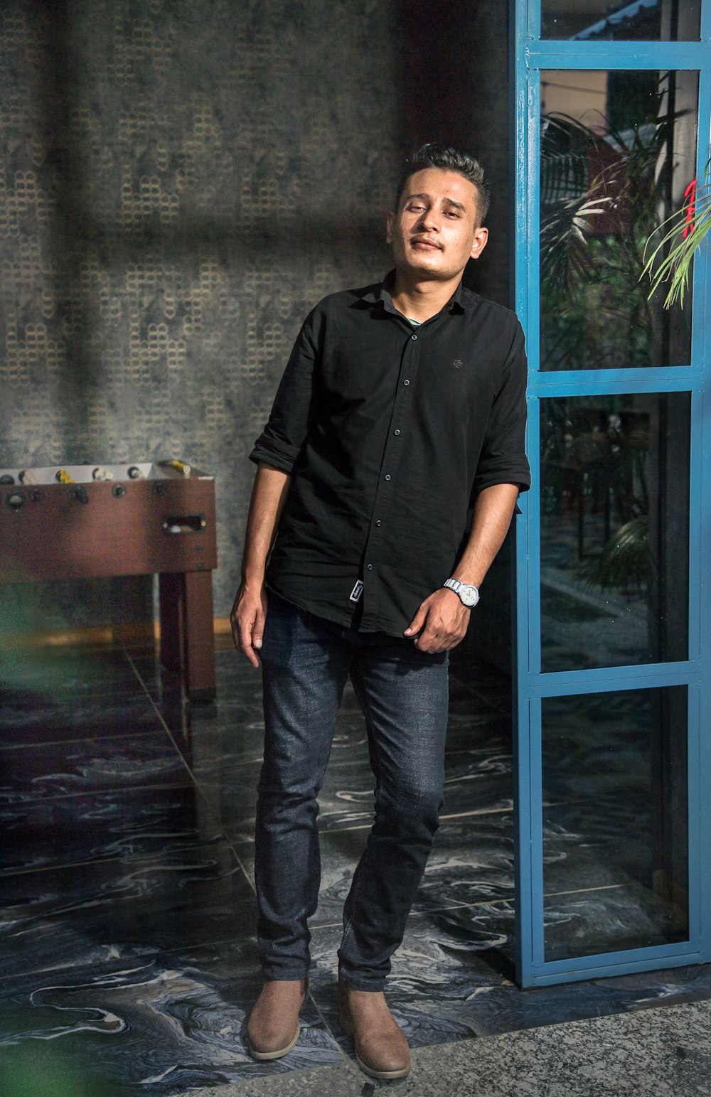 man in black button up shirt and black pants standing beside blue wooden framed glass door