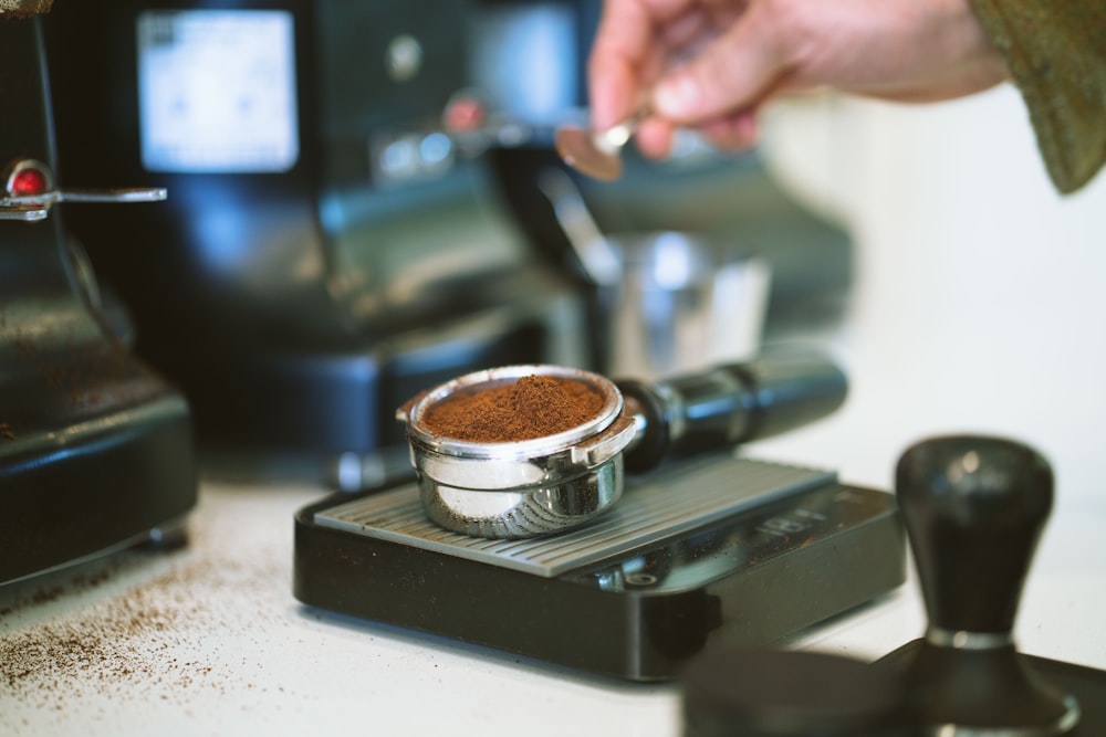 Persona sosteniendo una cafetera plateada y negra