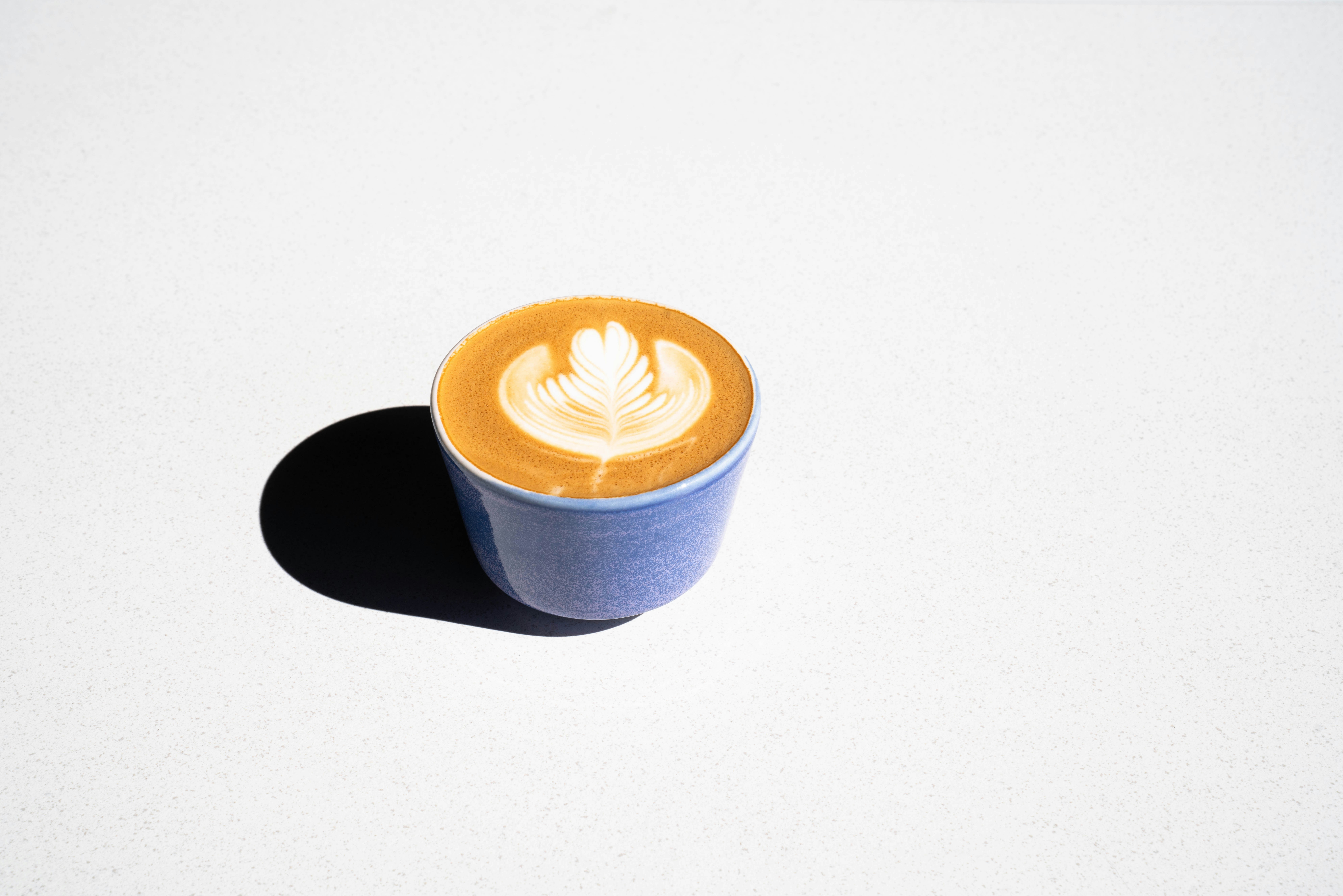 Latte with heart art in a blue cup on white