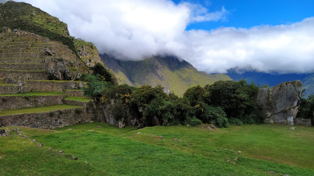 green grass field near green mountain under white clouds during daytime