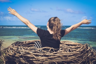 woman in black shirt sitting on brown wooden log near body of water during daytime