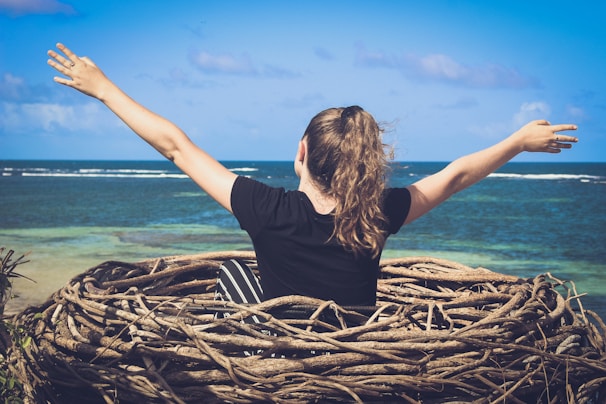 woman in black shirt sitting on brown wooden log near body of water during daytime