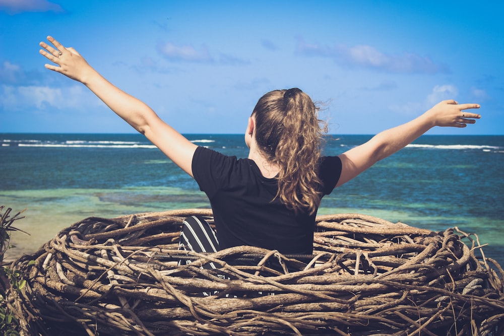 woman in black shirt sitting on brown wooden log near body of water during daytime