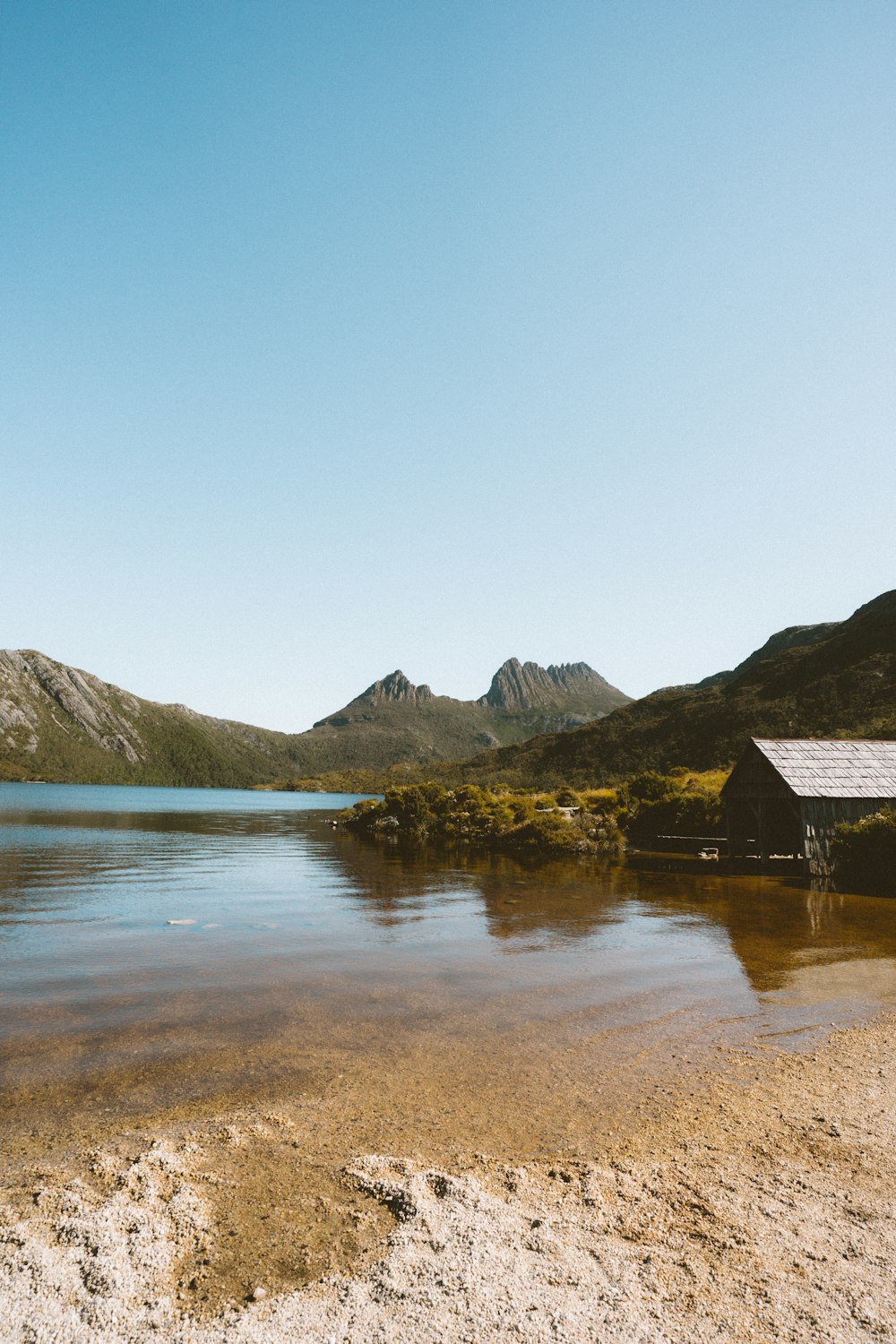 brown wooden house near lake and mountains during daytime