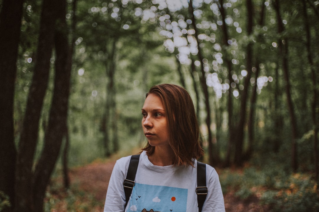 woman in white and blue crew neck shirt standing near green trees during daytime