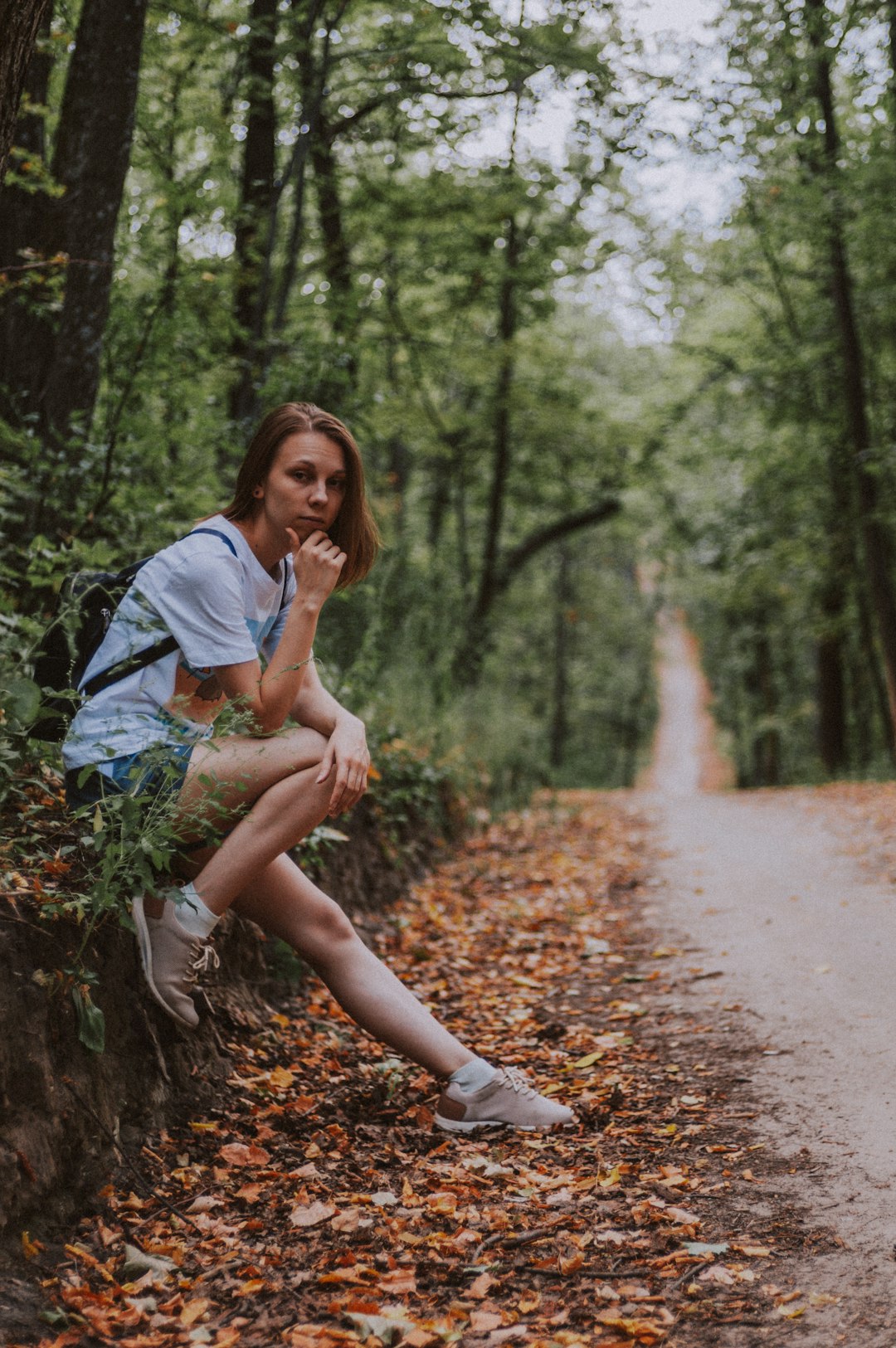 woman in white shirt sitting on brown dried leaves on pathway during daytime