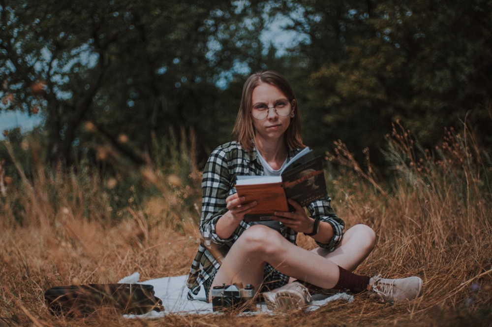 woman in black and white plaid dress shirt sitting on dried grass