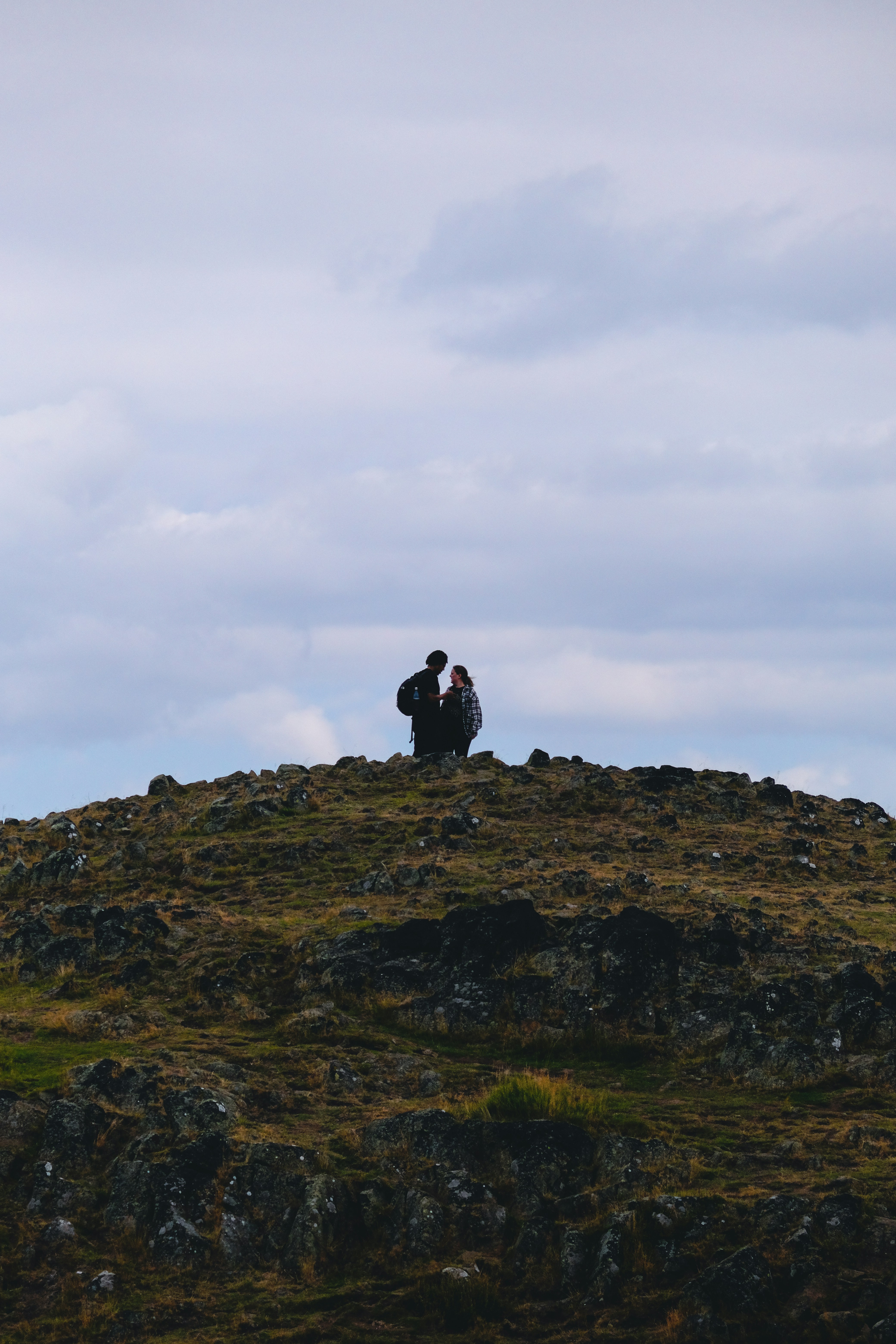 2 person sitting on rock formation under white clouds during daytime