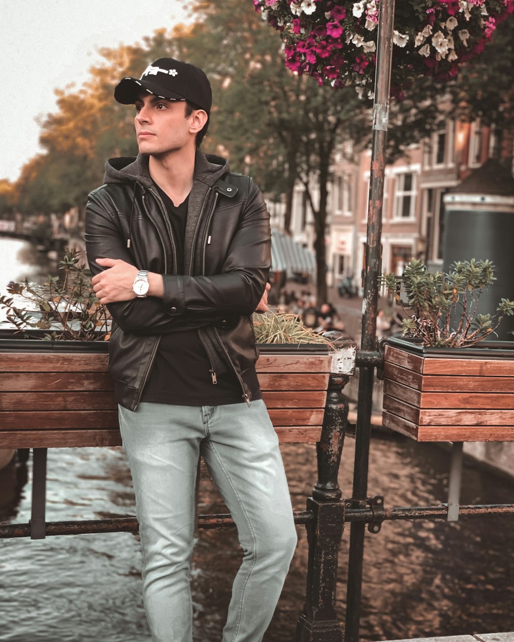 man in black leather jacket and gray pants standing near brown wooden bench during daytime