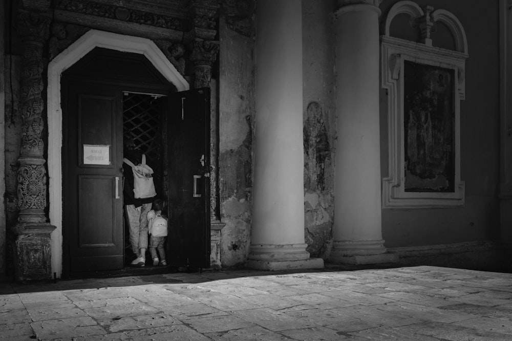 grayscale photo of man in black jacket standing near door