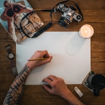 person holding white printer paper near black dslr camera and white ceramic mug