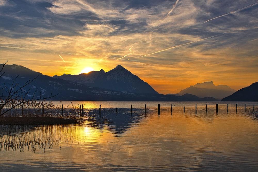 silhouette of mountain near body of water during sunset