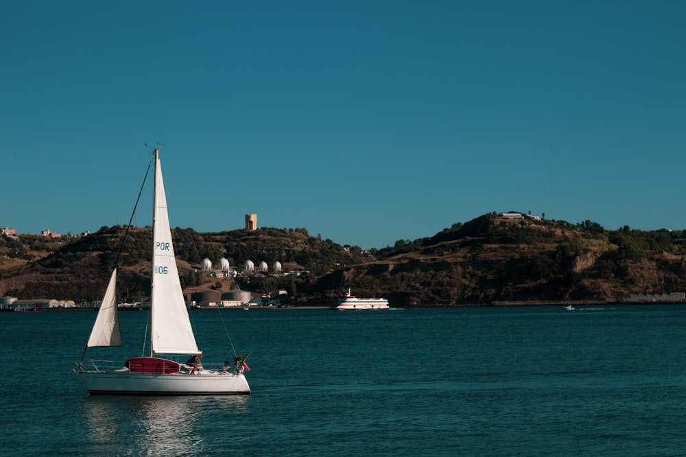 white sailboat on sea near brown mountain under blue sky during daytime