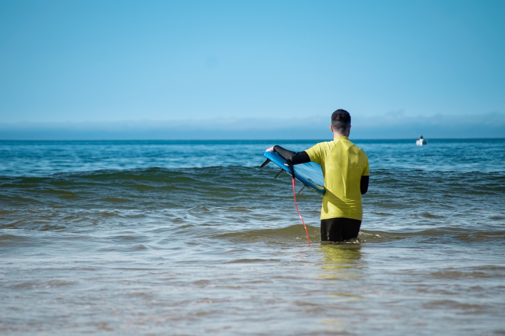 man in yellow and black wet suit holding red and black stick on sea during daytime