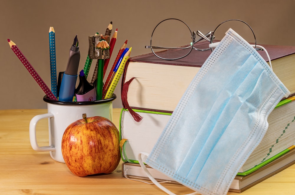 an apple, a book, a face mask, and a pair of glasses are