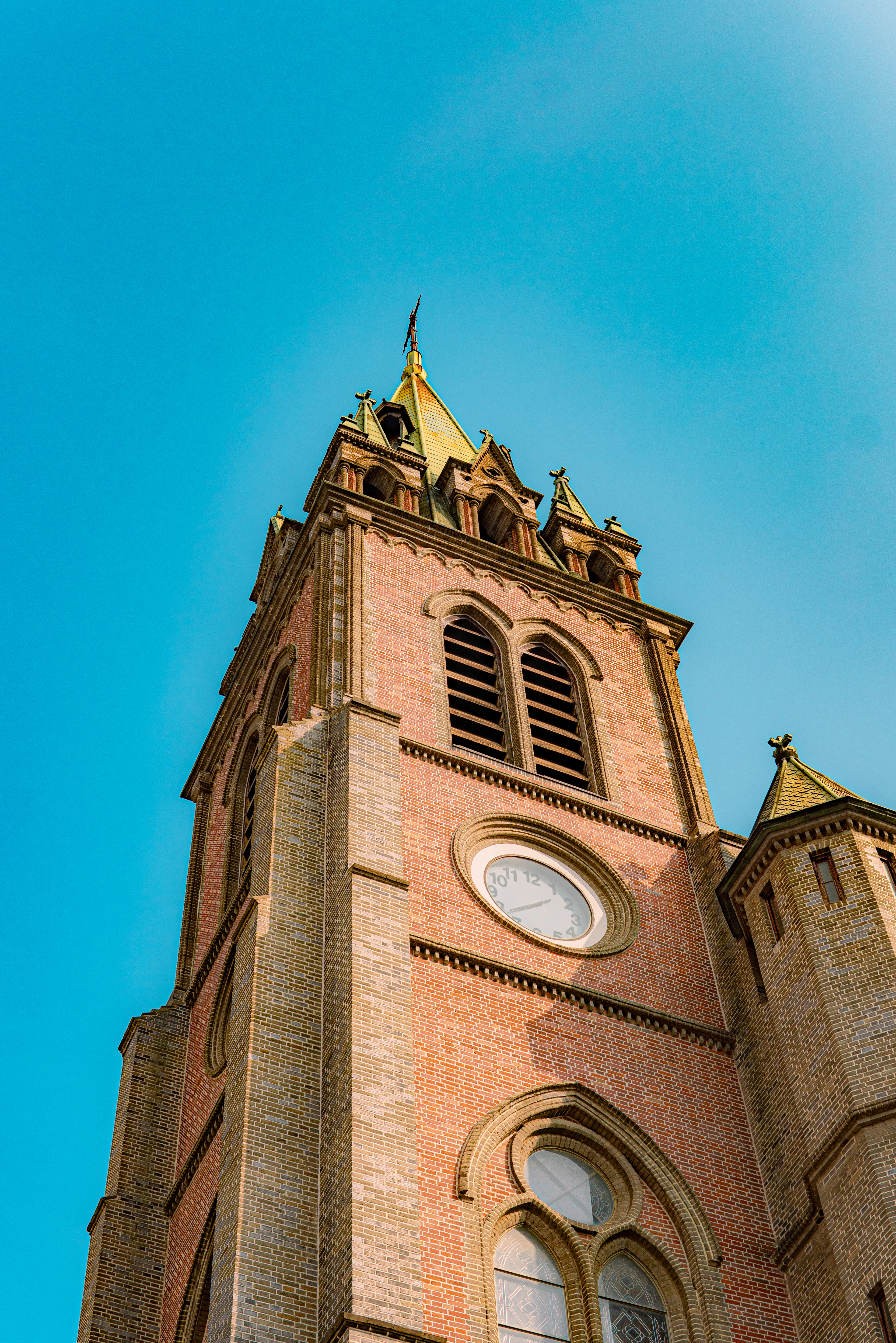 A red-brick Gothic clock tower with pointed spires rises against a clear blue sky.