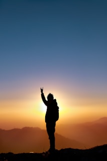 silhouette of man raising his hands during sunset