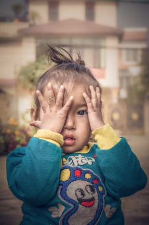 child in blue sweater covering face with yellow textile
