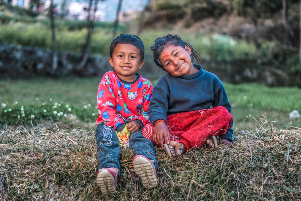 2 boys sitting on grass field during daytime