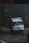 A large, colorful truck with various inscriptions and decorations is navigating a rough, dirt path on a foggy day. The words 'ROAD KING' are prominently displayed on the bumper, and the truck appears to be traveling in a mountainous region surrounded by dark, rocky terrain.