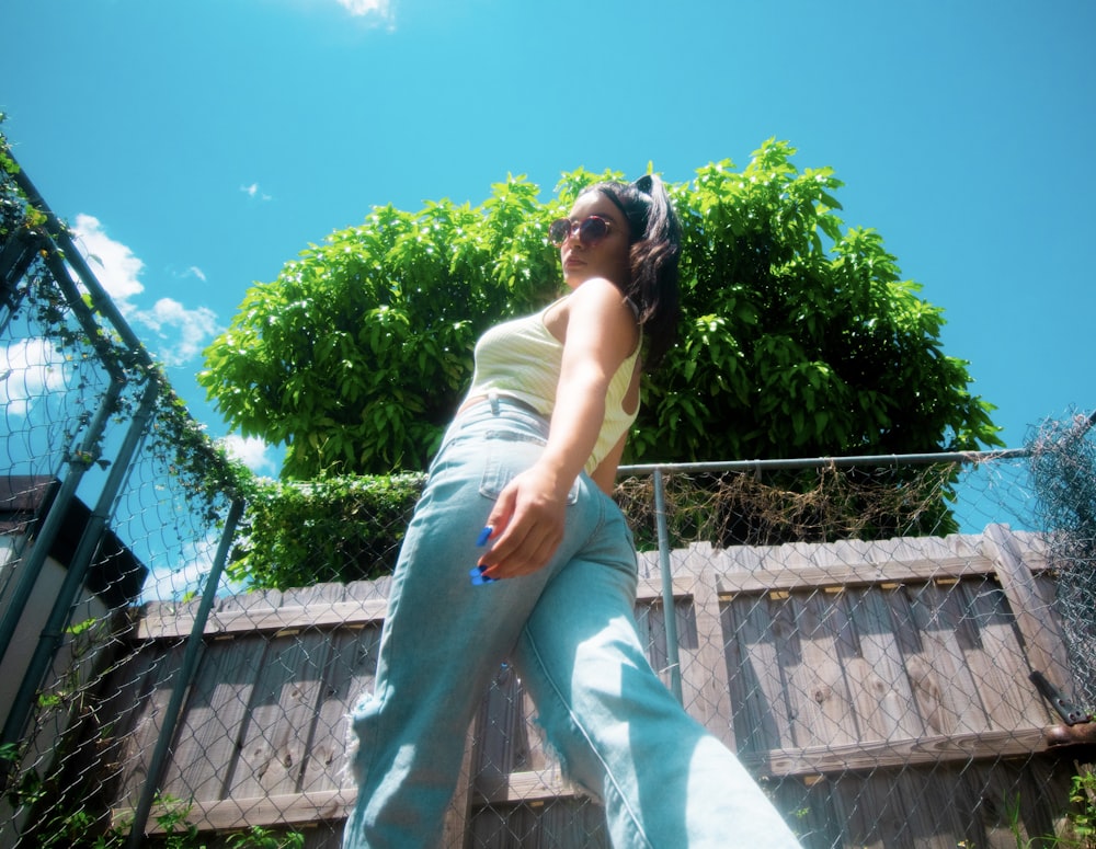 woman in white tank top and white pants sitting on gray concrete fence during daytime