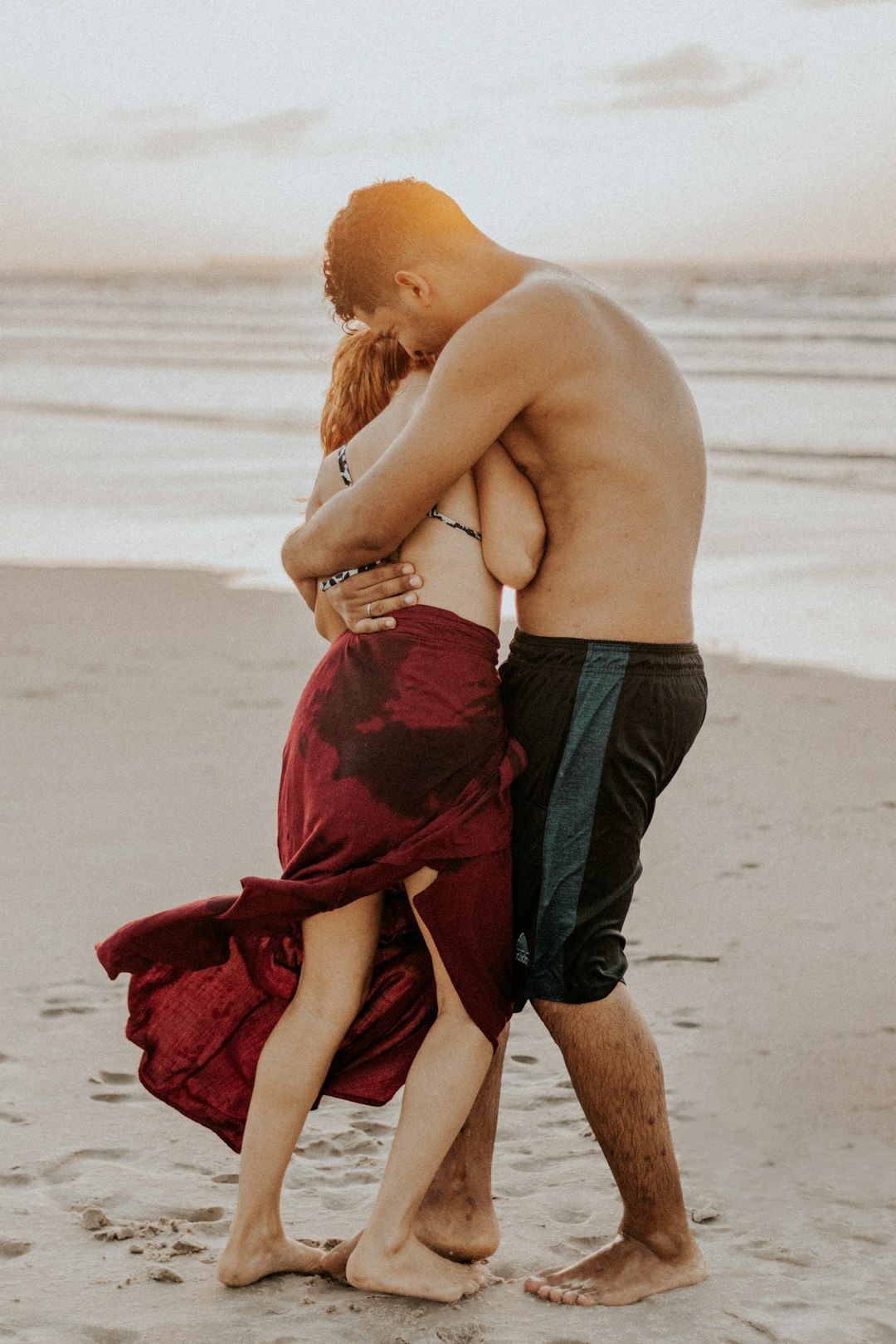 man in black shorts holding woman in red dress on beach during daytime